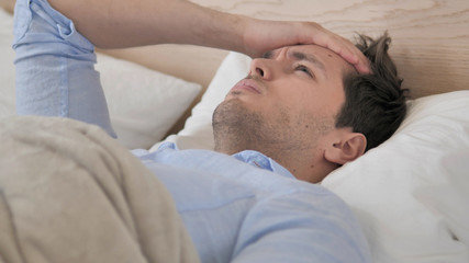 Tense Young Man with Headache Lying in Bed