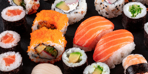 Large sushi set panoramic close-up on a black background. An assortment of various maki, nigiri and rolls