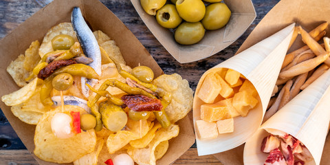 Tapas and pinchos panoramic overhead shot. Cheese, jamon and olives, gildas and sardines on a wooden table in an outdoors cafe