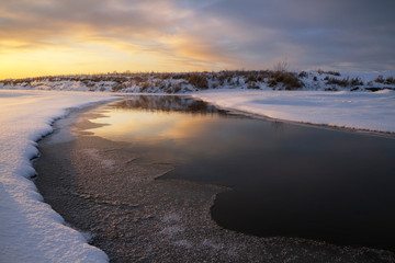 icy banks of a small river at sunset