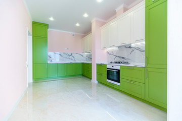 New kitchen set in green and white colors in the style of minimalism in a new building. The top under the marble. The doors in the cabinets are green. Beige walls. 