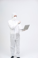 man wearing biological protective uniform suit clothing, mask, gloves spraying sanitizer on computer for sanitizing virus bacteria