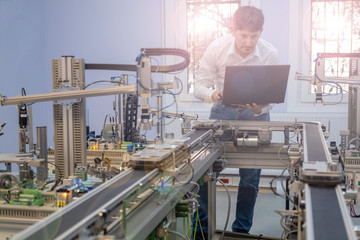 Engineer is working on laptop to program smart factory prototype's automation. automated car on production line, artificial intelligence in smart manufacturing. Industry 4.0 concept.	