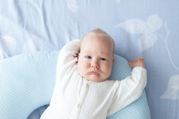 a three-month-old baby lies on a pillow with his hands up in the daylight