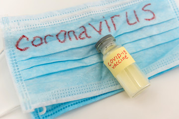 Coronavirus as danger disease. COVID-19 write on blue medical face mask and virus vaccine ampoule