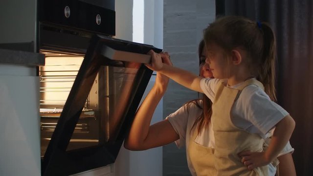 The Family Cooks Together. Mother And Daughter Put The Pie In The Oven And Close The Door. Watch And Wait For Homemade Pizza Cooking. Happy Childhood, Help Your Mother.