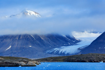 Travel in the Arctic. Dark winter mountain with snow, blue glacier ice with sea in the foreground, Svalbard, Norway.