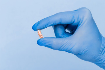 A hand in a blue medical glove holds one pill on a blue background. Disease Prevention Treatment