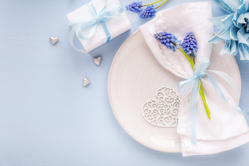 Fototapeta na wymiar Table place setting with a plate and a folded napkin decorated with blue spring flowers and ribbon. Mother's Day or Wedding dinner concept