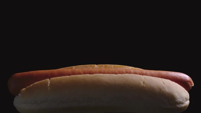 Sausage falling into a white bread. Hot dog cooking. Black background. Slow motion.