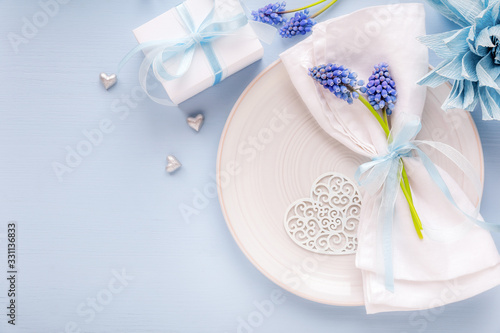 Table place setting with a plate and a folded napkin decorated with blue spring flowers and ribbon. Mother's Day or Wedding dinner concept