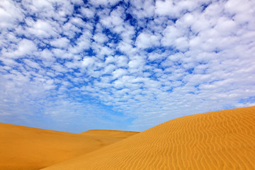 Summer dry landscape in Africa. Black pebble stones. Sandy waves in the wild nature. Dunas Maspalomas, Gran Canaria, Spain. Beautiful rare blue sky with white clouds.