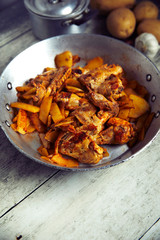 Spicy chicken wings with curry and potatoes, into a iron pot, wood background, top view