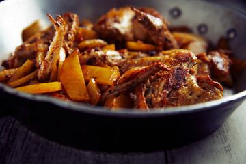 Spicy chicken wings with curry and potatoes, into a iron pot, wood background, close up