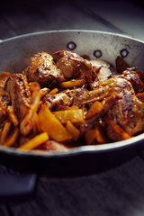 Spicy chicken wings with curry and potatoes, into a iron pot, wood background, close up