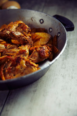 Spicy chicken wings with curry and potatoes, into a iron pot, wood background, close up