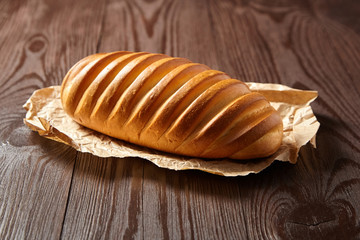 Bakery product. Baked whole bun on wooden table. Loaf, white wheat bread on baking paper on brown background