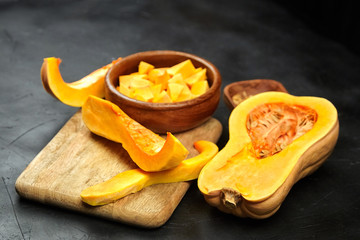 Butternut squash pieces, wooden bowl with pumpkin seeds, cutting board on black background, closeup. Cooking winter squash