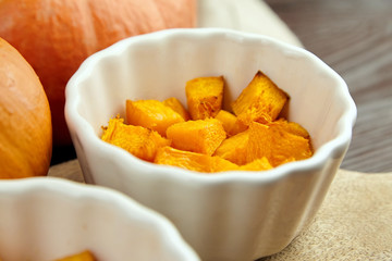 Pieces of baked pumpkin in white ceramic bowl on wooden background