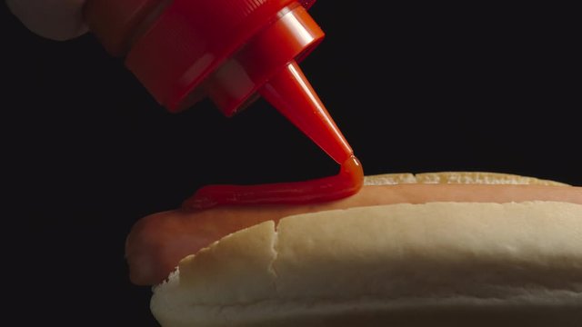 CLOSE UP: Ketchup bottle pouring tomato sause on a hot dog with sausage. Side view