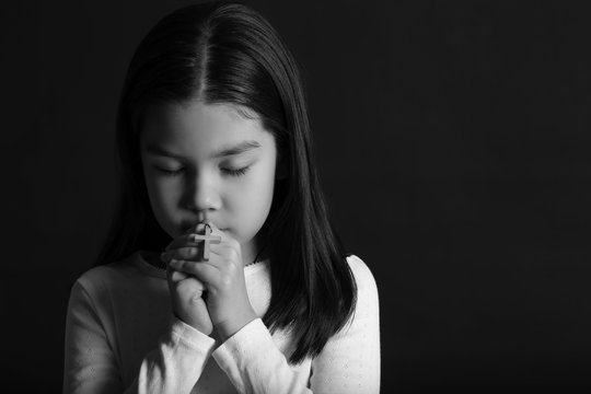 Black and white portrait of cute little Asian girl praying on dark background