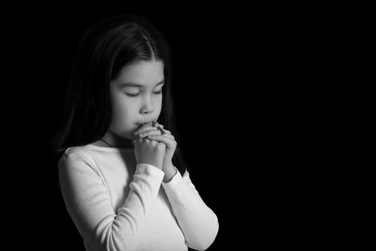 Black and white portrait of cute little Asian girl praying on dark background