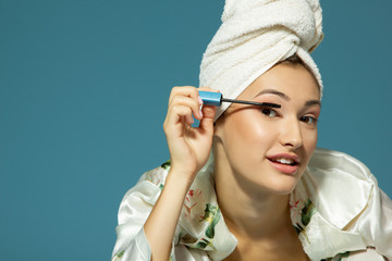 young attractive woman putting eye mascara over blue background, beauty treatment morning