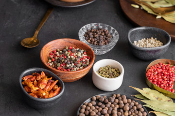 Different  pepper type, black ,white, pink ,green, cayenne, allspice peppercorns and bay leaf in bowls on dark background.
