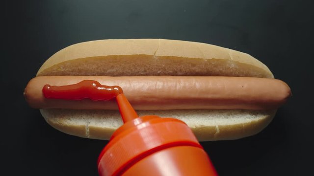 TOP VIEW: Ketchup bottle pouring tomato sause on a hot dog with sausage