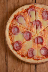 Flat lay pepperoni pizza isolated on rustic wooden background. Pizza salami cut in slices. Fast food, junk food concept.