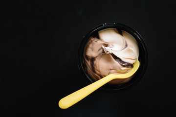 top view of an ice cream on a black table. Chocolate, vanilla and hazelnut flavoured soft ice cream with yellow spoon