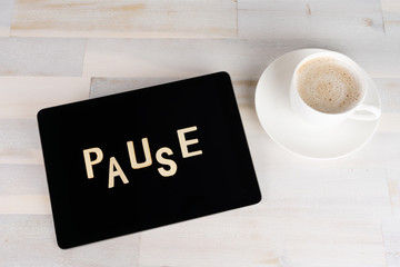 A tablet computer with the german word for break on a wooden table, next to it a cup of coffee