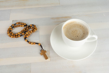 A rosary on a wooden table, beside a cup of coffee