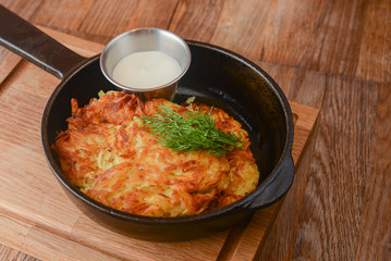 Delicious potato pancakes with cheese and herbs in a pan over light rustic wooden board. Dinner in restaurant.