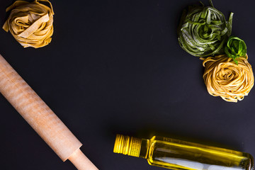 Italian spaghetti ingridients on a black background with bottle of olive oil and rolling pin.