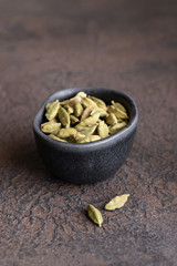 Cardamom seeds in black bowl concrete background. Aromatic herb and Spicy Seasoning for cooking concept.