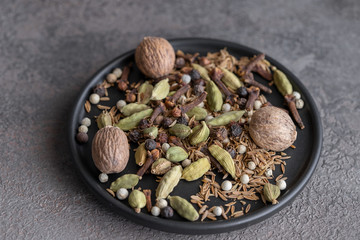 Garam masala in black plate on cocrete background. Indian blend of ground spices used in Asian cuisines and in Ayurvedic medicine.