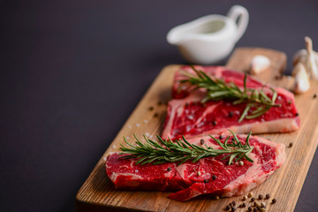 Fresh raw steak on wooden cutting board over black background with spices, top view.