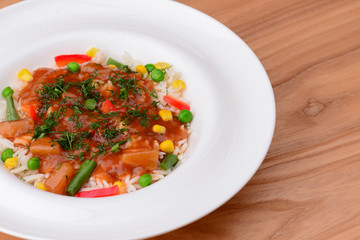 Rice with beef stew with green beans and vegetables served in white plate over light rustic wooden table.