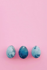 Natural dyed blue colored eggs on pastel pink background, top view.