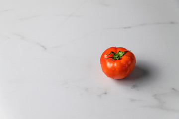 Fresh ripe tomato on light marble background with copy space. Summer organic vegetable for salad