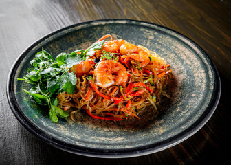Stir fry noodles with vegetables and shrimps in plate on wooden table background