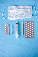 Still life : Medical mask, pills, thermometer, syringe on a blue background