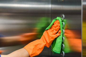 Woman hand in protective orange rubber gloves holding green microfiber cleaning cloth and wiping...