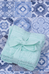 Stacked green face towels flannels tied with ribbon and a bow.  On a blue patterned tiled surface