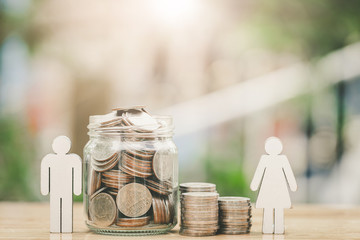 Elderly couple made from wooden blocks place side pile of coins . Saving, retirement, investment planing concept with blurred green nature as background.