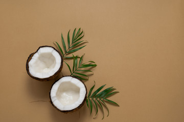 top view halves of coconut and green tropical leaves on a brown background copy space