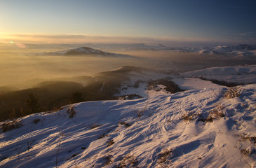 Winter sunset snow mountain view on the background of hills under colorful sky