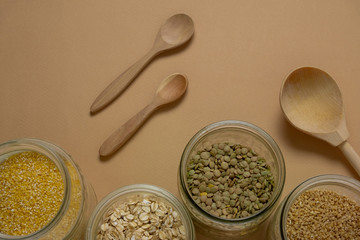 dry cereals in glass jars and wooden spoons top view on a beige background , zero waste kitchen...