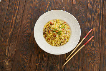 Fried rice with vegetables and beef in white plate, chopsticks on wooden background, Asian food concept, top view copy space